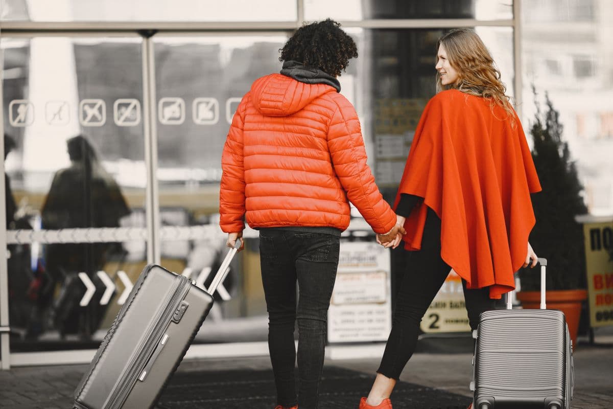 Casal estiloso de mãos dadas com as malas, a caminho da viagem